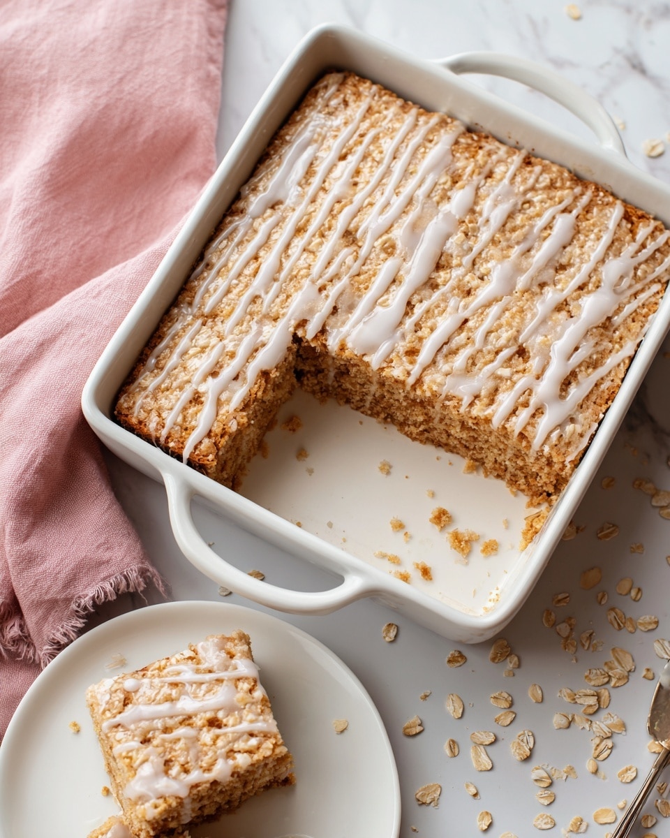 A square piece of baked oat bar with a textured top covered in light drizzle of white icing sits in the center of a white plate. The oat bar is golden-brown with visible oats and a slightly rough surface. The white icing is spread across the top, some pooling slightly around the base. A gold fork rests on the plate with its tines partially under the oat bar. Next to the plate is a white baking dish with a bigger portion of the same oat bar, showing a missing square where the piece was taken out. The oat bar inside the dish has the same golden oat texture and white icing drizzle. Scattered oats are visible on a pink cloth and a white textured towel all placed on a white marbled background. Photo taken with an iphone --ar 4:5 --v 7