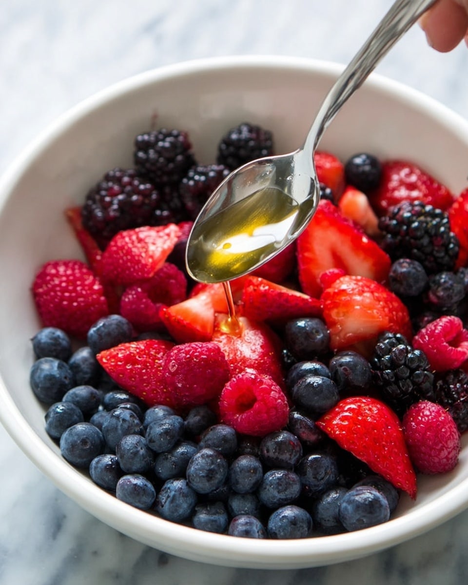 A close-up view of a white bowl filled with mixed berries, showing three main layers: the bottom layer has whole blueberries in dark blue with a smooth texture, the middle layer is made of bright red strawberries with bumpy seeds and some cut in half showing their juicy red inside, and the top layer has blackberries and raspberries with their rough and bumpy textures in black and red colors. A silver spoon held by a woman's hand is dripping honey over the berries, with the honey being light golden and syrupy. The bowl is placed on a white marbled surface. photo taken with an iphone --ar 4:5 --v 7