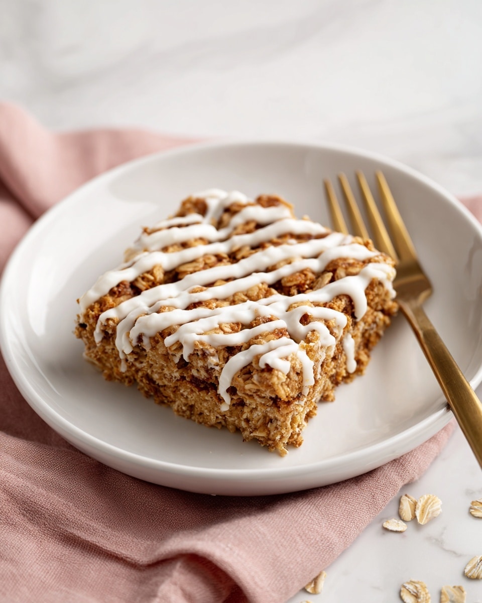 A square piece of oatmeal bake sits on a white plate, showing a rough, soft texture made of oats with visible whole flakes and a brownish mix, indicating cinnamon or spices inside. The top layer is drizzled with a white icing in uneven lines that contrast with the warm brown oat surface. A gold fork rests on the plate beside the oatmeal bake, with a soft pink cloth underneath the plate adding a gentle color touch. The plate is placed on a white marbled surface with some oats scattered around. Photo taken with an iphone --ar 4:5 --v 7