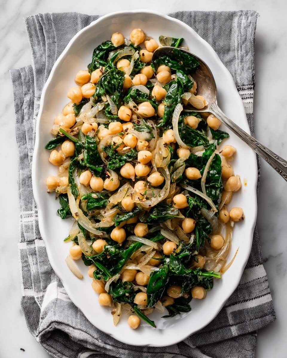 The dish shows a close-up of cooked chickpeas mixed with dark green wilted leafy vegetables and soft, translucent pieces of onion. The chickpeas are pale yellow and round, evenly spread throughout the white bowl. The dark green leaves are scattered in between, adding texture and depth. The translucent onion pieces are placed on top and among the chickpeas, showing a light brown tint. A silver spoon rests in the bowl, scooping up some chickpeas and greens. The bowl sits on a white marbled surface. photo taken with an iphone --ar 4:5 --v 7