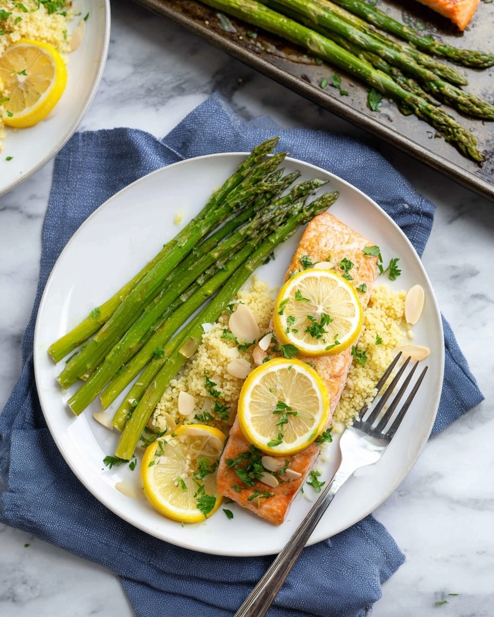 On a white plate, there is a piece of cooked salmon topped with two thin yellow lemon slices and sprinkled with chopped green herbs. Next to the salmon are several long green asparagus stalks, placed in a neat line. To the right of the asparagus, there is a serving of light yellow couscous mixed with small almond slices and decorated with additional lemon slices and green herbs. A silver fork rests on the plate near the bottom edge. The plate sits on a blue cloth over a white marbled surface, with a dark baking tray holding more asparagus and a piece of salmon visible in the upper left corner. Photo taken with an iphone --ar 4:5 --v 7