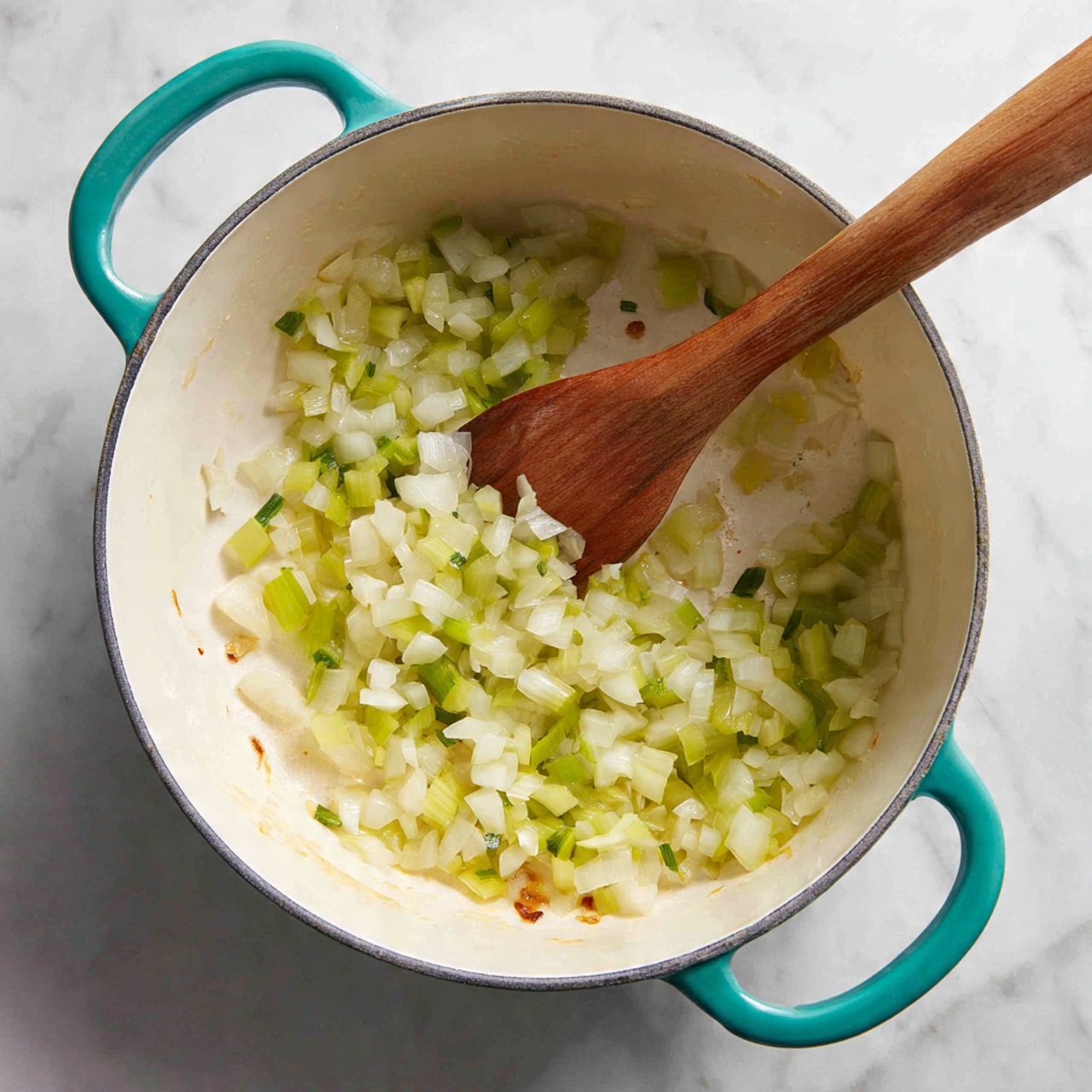 A white cooking pot with bright teal handles holds a mix of cooked small chopped onions and celery, showing a translucent pale yellow and light green color with a soft, slightly wet texture. A wooden spatula with a long handle is partially resting inside the pot, stirring the mixture. The pot’s white interior contrasts with the clear and shiny vegetable pieces, while some brown bits stick lightly to the sides near the bottom. The pot is placed on a white marbled surface. photo taken with an iphone --ar 4:5 --v 7