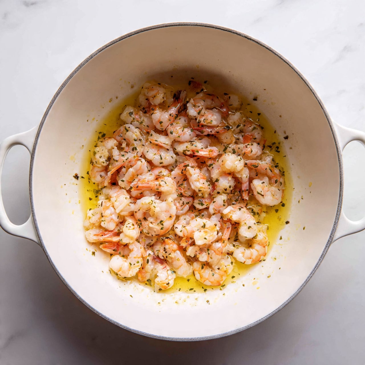 Inside a white cooking pot, there is a pile of small shrimp pieces with a mix of pink and light orange colors. The shrimp look cooked and are sitting in a thin layer of yellow oil or butter that spreads across the bottom of the pot. The texture of the shrimp is soft and slightly shiny, with some parts appearing more browned than others. The pot is set against a white marbled surface. photo taken with an iphone --ar 4:5 --v 7