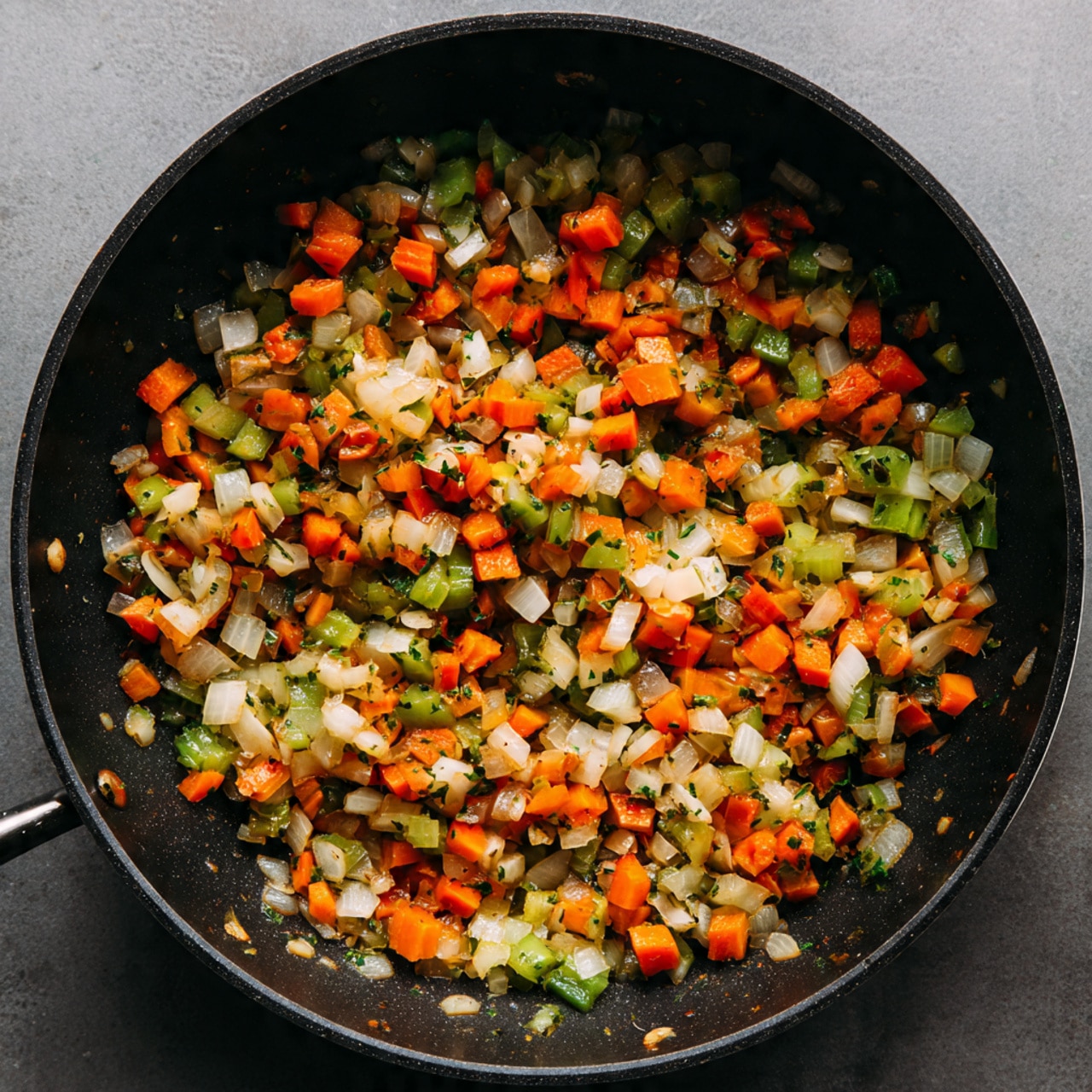 This image shows a black pan filled with small pieces of cooked vegetables, including orange carrots, white onions, green celery, and red bell peppers, all mixed together. The vegetables have a soft texture with some slight browning, indicating they have been sautéed. The colors are bright and vivid, spread evenly across the bottom of the pan with no space uncovered, showing a fresh and warm look. The pan's inside is matte black, contrasting with the colorful vegetables. Photo taken with an iphone --ar 4:5 --v 7