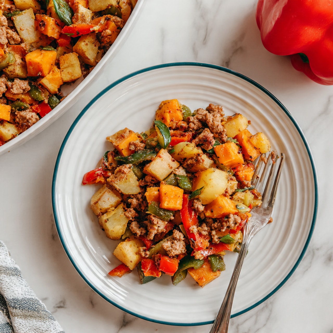 The dish shows a single layer of cooked ground meat mixed with diced vegetables in a white skillet. The vegetables include orange sweet potatoes, light yellow potatoes, and red and green bell peppers, all cut into small cubes with a soft texture. The food is lightly sprinkled with chopped green herbs, giving a fresh color contrast to the warm tones of the vegetables and meat. To the right, a wooden spoon holds a small serving of the same mixture. On the left side, there are two silver forks resting on a white cloth with gray patterns, placed on a white marbled surface. The lighting is bright and natural, making the colors fresh and clear. photo taken with an iphone --ar 4:5 --v 7