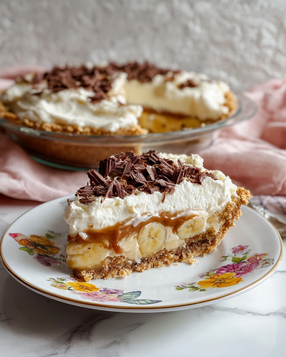 The image shows a round pie in a clear glass dish on a white marbled surface with a soft pink cloth nearby and a spoon to the side. The pie has three visible layers: the bottom layer is a golden brown crumbly crust, the middle layer is a smooth caramel or butterscotch filling with a light brown color, and the top layer is a thick, fluffy white whipped cream spread unevenly with a soft texture. On top of the whipped cream, there are random dark brown chocolate shavings scattered. The whole scene is bright and clean, with natural light making the textures and details clear. Photo taken with an iphone --ar 4:5 --v 7