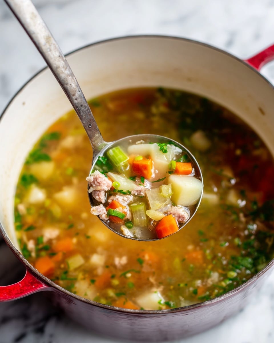 A white pot with a red handle holds a clear, light brown soup filled with colorful pieces. The soup has multiple layers: the bottom is light brown broth with floating bits of fresh green herbs, small orange carrot cubes, green celery chunks, pale green cabbage pieces, light pink shredded meat, and small round light brown potato pieces. A metal ladle is lifted from the pot, holding a mix of these ingredients, showing the different colors and textures close up. The background is a white marbled surface. photo taken with an iphone --ar 4:5 --v 7
