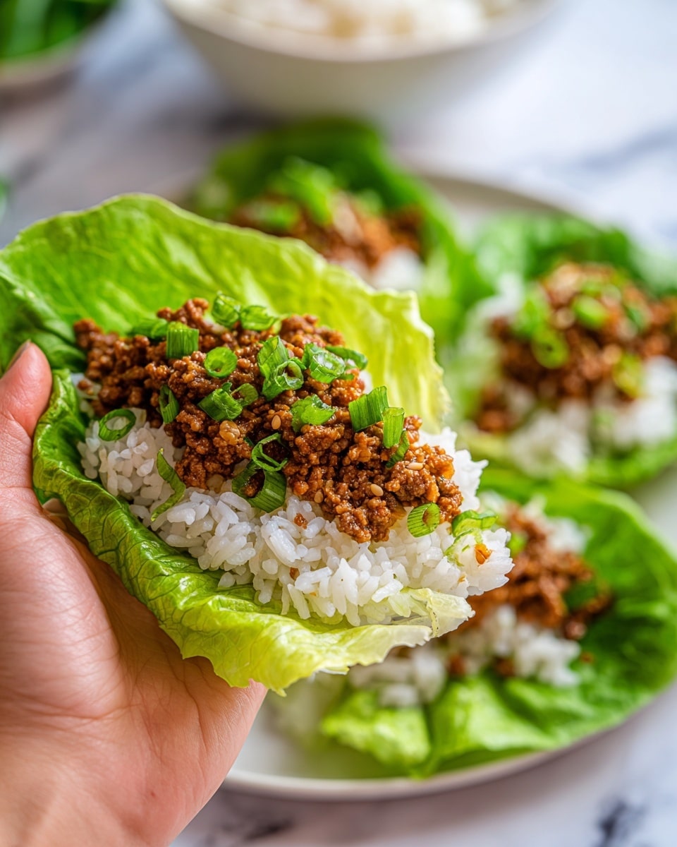 A close-up image shows a woman's hand holding a fresh green lettuce leaf shaped like a small cup, filled with white rice at the bottom layer, topped with crumbled cooked ground meat that has a rich brown color and a slightly crumbly texture. On top of the meat, small green onion pieces are scattered. In the background, more lettuce wraps sit on a white plate on a white marbled surface, with a blurred bowl of rice visible. The colors are vibrant with bright green from the lettuce and onions, pure white from the rice, and deep brown from the meat, all presented in a fresh and clean way photo taken with an iphone --ar 4:5 --v 7