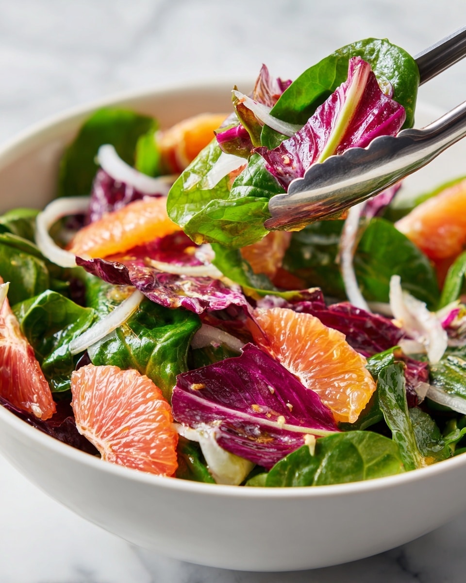 A white bowl filled with a colorful salad showing multiple layers: at the bottom, fresh green spinach and bright purple radicchio leaves, mixed with small pieces of pink grapefruit and thin slices of white onion with a touch of dressing giving a slightly shiny texture. A pair of silver salad tongs lift a portion, highlighting the mix of leafy greens and grapefruit chunks. The white marbled surface is blurred in the background. Photo taken with an iphone --ar 4:5 --v 7