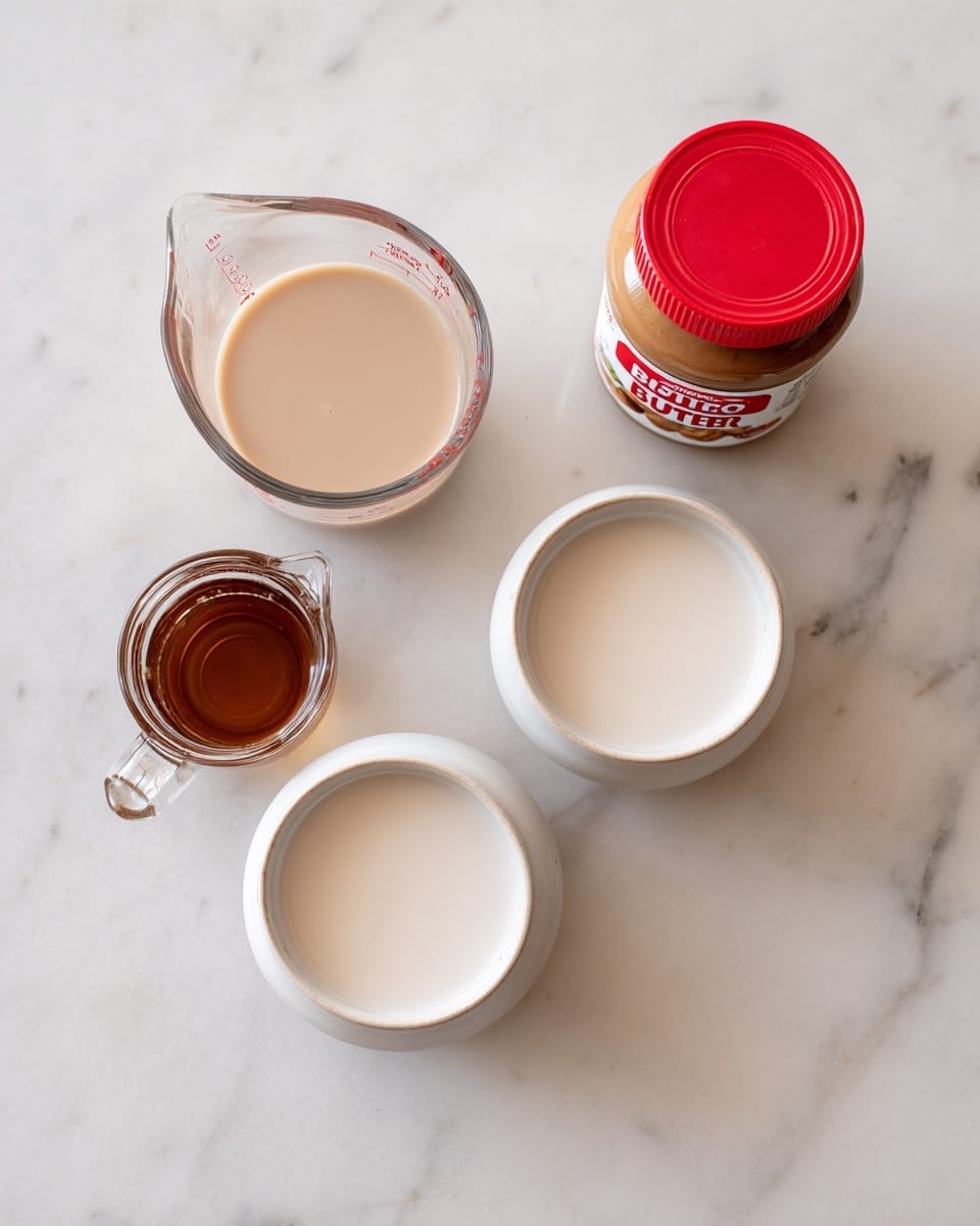 A clear glass measuring cup with light creamy liquid at the top left, two small white ceramic bowls each filled with a white liquid positioned side by side in the center and bottom right, a small clear glass pitcher with a brown liquid at the bottom left, and a jar of Biscoff creamy cookie butter with a red lid placed on its side on the top right, all arranged on a white marbled surface. photo taken with an iphone --ar 4:5 --v 7