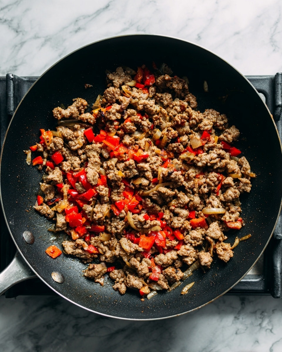 A close-up view of a black non-stick pan on a stove with ground meat cooked lightly brown mixed with small pieces of red bell pepper, and some bits of onion. The meat pieces are uneven and scattered throughout the pan, and the red pepper pieces add bright spots of color. The stove grates are visible around the pan, and the background is a white marbled texture. photo taken with an iphone --ar 4:5 --v 7