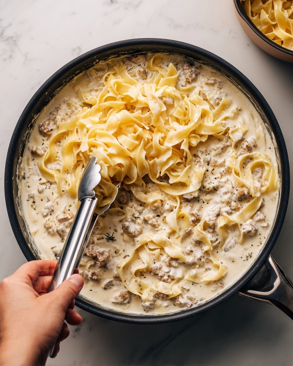 The image shows a close-up view of a frying pan filled with creamy white sauce mixed with light brown, tender pieces of cooked meat. The sauce is thick and smooth, covering most of the meat pieces which are scattered unevenly throughout the pan. The pan has a black interior with some sauce spread around the edges. The background is a white marbled texture visible at the edges of the pan, giving a clean and bright look to the setup. photo taken with an iphone --ar 4:5 --v 7