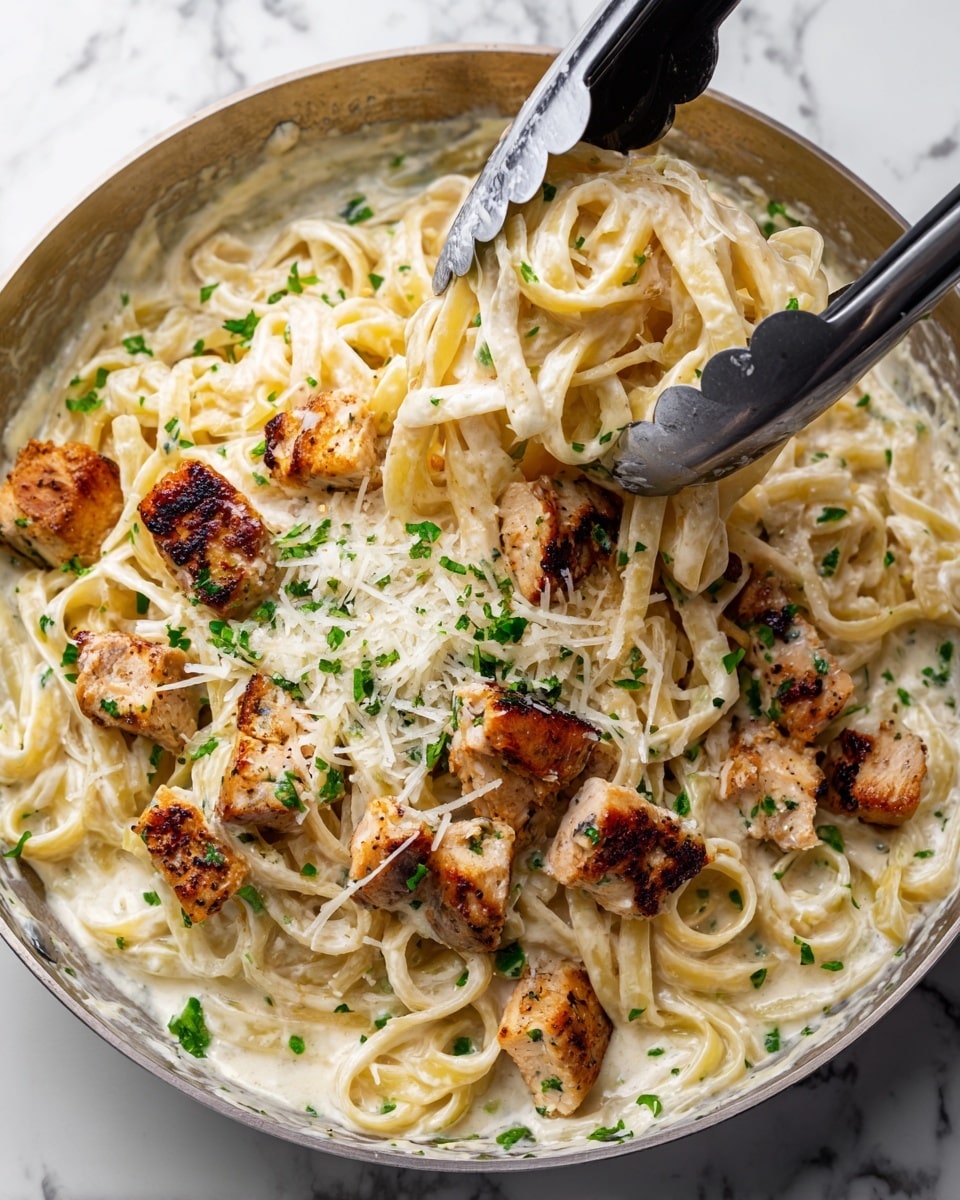 The image shows a dish with two layers: the bottom layer is creamy white pasta coated in a smooth, light-colored sauce, and the top layer is pieces of golden-brown grilled chicken arranged above the pasta. The chicken pieces have a slightly charred texture with a mix of light and dark brown colors and are cut into thick strips. Small green herb bits are sprinkled on both the pasta and chicken, and finely grated cheese is scattered across the top. The dish is placed on a white plate over a white marbled surface. Photo taken with an iphone --ar 4:5 --v 7