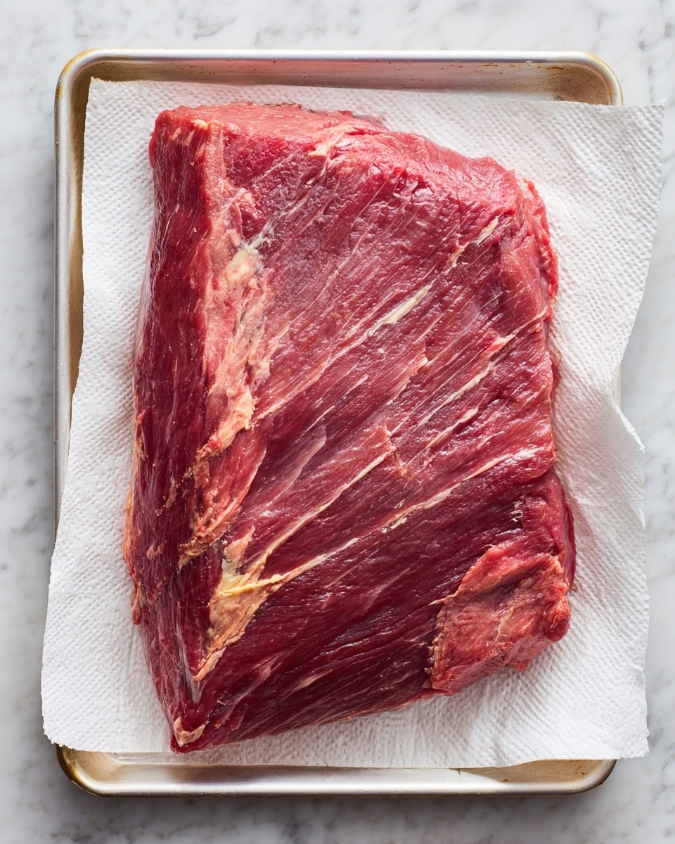 A large single layer of raw beef brisket laid flat on a baking tray lined with white paper towels, the meat showing a mix of deep pink and light marbled white fat streaks along its uneven surface, highlighting its fibrous texture and natural grain. The edges appear slightly thicker with some patches of thicker fat, while the center shows a smoother cut. The tray rests on a white marbled surface. photo taken with an iphone --ar 4:5 --v 7