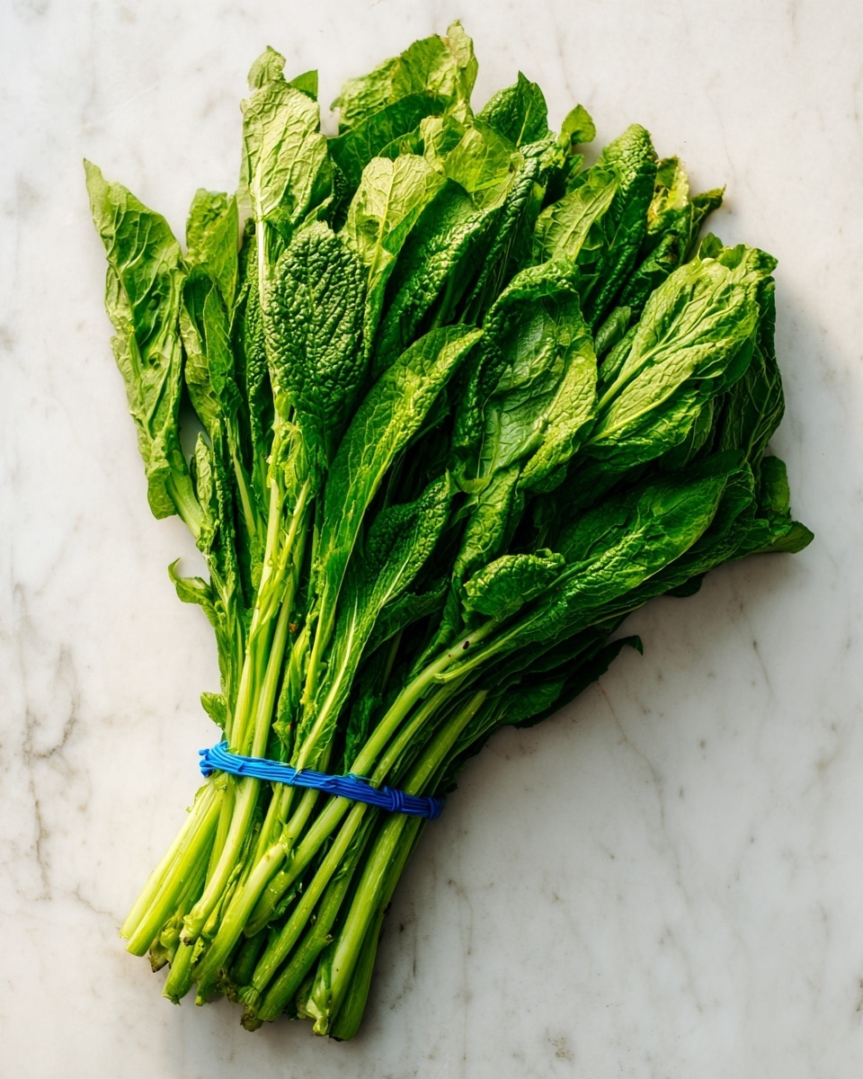 The image shows a large bunch of fresh green leafy vegetables lying flat on a white marbled surface. The leaves are vibrant and dense, with long green stems tied together with a blue band on one side. The leaves have a textured, slightly ruffled look, and the bunch spreads out broadly from the tied area. There is natural light casting soft shadows around the edges, highlighting the freshness and fullness of the greens. photo taken with an iphone --ar 4:5 --v 7