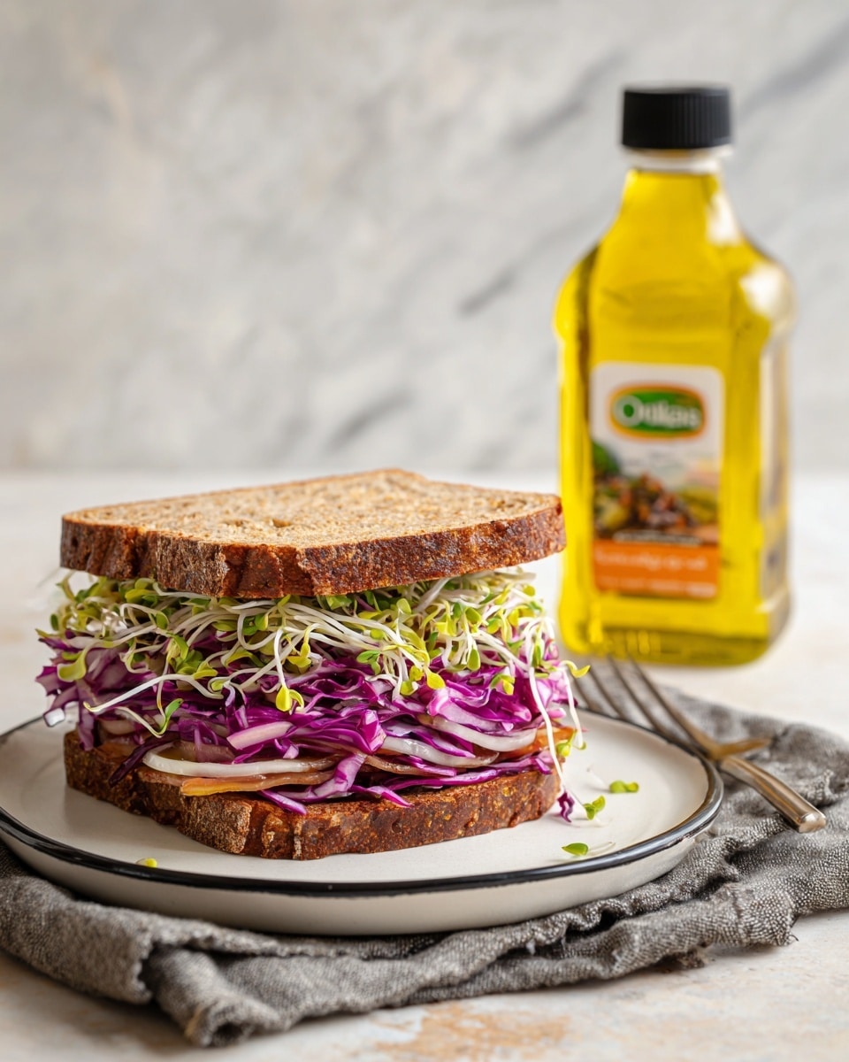The image shows a sandwich on a white plate with a black rim, placed on a gray cloth on top of a white marbled surface. The sandwich has three visible layers: the top layer is a thick, dark brown bread, the middle layer is filled with purple cabbage and thin white onion slices mixed with green sprouts, and the bottom layer appears to be a lighter bread slice. Next to the plate, there is a clear bottle of yellow safflower oil with a black cap and an orange and white label. photo taken with an iphone --ar 4:5 --v 7