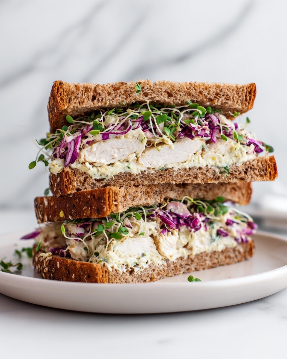 A sandwich on two slices of dark brown oat bread with visible oats on the crust. The bottom layer has a bed of green leafy sprouts, topped with a thick piece of golden-brown seasoned patty. Above the patty, there is a colorful layer of shredded cabbage mix with light purple and pale green colors, giving a fresh look. More green sprouts are placed on top of the cabbage, all stacked inside the sandwich. The sandwich sits on a white plate with a black rim, on a white marbled surface with a blurred background. photo taken with an iphone --ar 4:5 --v 7