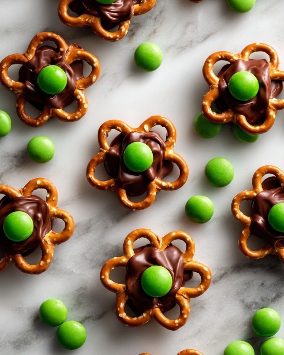 The image shows several flower-shaped snacks made with light brown pretzels forming five petal loops around a dark brown chocolate center. In the middle of the chocolate, there is a green candy. The flowers are placed on a white marbled surface with scattered green candies around them. photo taken with an iphone --ar 4:5 --v 7