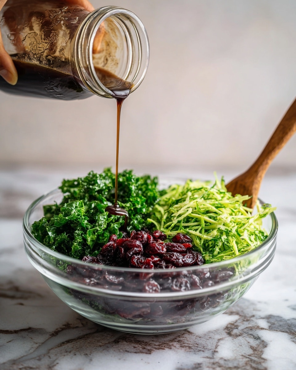 A clear glass bowl sits on a white marbled surface filled with three main layers: bright green shredded leafy vegetables on the right, dark green chopped kale on the top left, and a pile of deep red dried cranberries on the bottom left. Above the bowl, a woman's hand holds a glass jar tilted downward, pouring a thin stream of dark brown dressing into the bowl. A wooden spoon is partially visible resting inside the bowl on the right side. The background is softly blurred with a light neutral tone. photo taken with an iphone --ar 4:5 --v 7