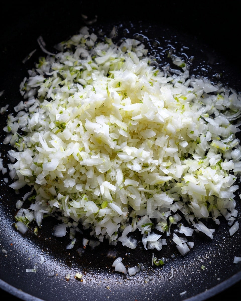 A close-up top view of finely chopped white onions spread evenly in a single layer inside a black pot. The onions show small bits with some slight green parts visible, mixed with a glistening surface of oil or water reflecting light. The pot's interior is dark with a smooth texture, contrasting with the white and light green of the onions. The scene is simple and focused only on the onions cooking. Photo taken with an iphone --ar 4:5 --v 7