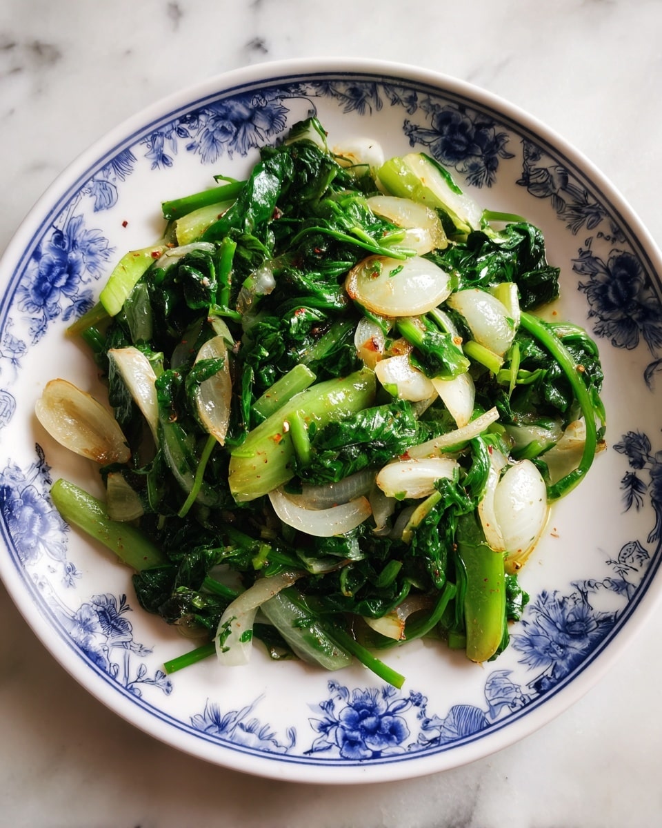 A close-up view of a black pan with cooked leafy greens and sliced onions inside. The dish has two main layers: a bottom layer of soft white onions with a translucent texture, and a top layer of bright green leafy vegetables that look shiny and slightly wilted from cooking. The greens have different shades of green, from light yellow-green to dark green, adding depth to the dish. The pan holds a small amount of liquid around the edges, making the dish look moist and fresh. The background shows a white marbled texture. photo taken with an iphone --ar 4:5 --v 7