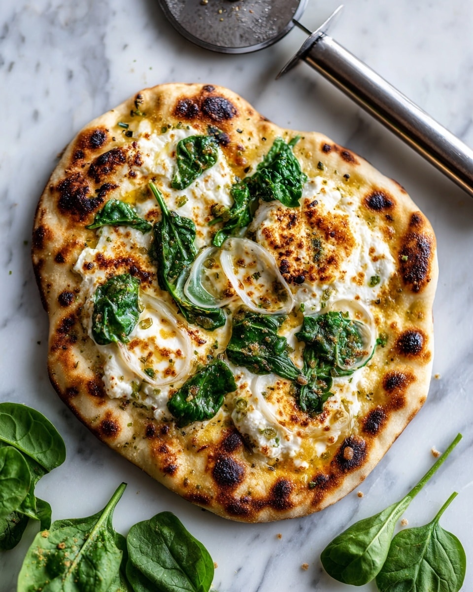 The image shows a small round flatbread divided into four triangular slices, placed on a dark slate surface with a pizza cutter beside it. The flatbread is golden brown with a slightly toasted edge and black sesame seeds visible in the dough. On top, there is a layer of melted white cheese, spread spinach leaves in dark green, thin white onion slices, and crumbled white cheese sprinkled evenly. Fresh spinach leaves lie on the side. The photo taken with an iphone --ar 4:5 --v 7