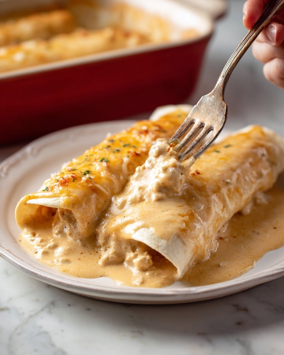 Two creamy enchiladas lie side by side on a white plate, bathed in a light golden tan sauce with a smooth texture. The enchiladas are soft and folded, the sauce slightly bubbling and thick, covering the tortillas completely. One enchilada is partially opened by a silver fork, revealing the creamy inner filling, which looks rich and soft with small chunks inside. The plate rests on a white marbled surface, with a blurred red baking dish visible in the background. A woman's hand holds the fork gently lifting the filling from the enchilada. photo taken with an iphone --ar 4:5 --v 7