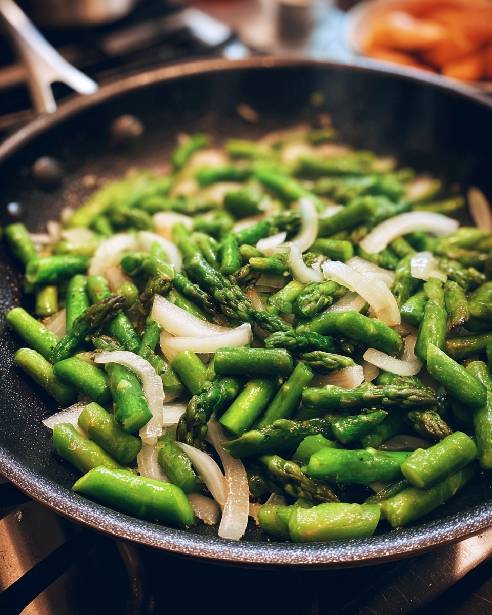 A black frying pan filled with chopped bright green asparagus pieces mixed with small, thin slices of translucent white onions, all cooking gently on a stove burner with a blurred background. The asparagus and onions are spread evenly across the pan's surface, showing a fresh and lightly sautéed texture. photo taken with an iphone --ar 4:5 --v 7