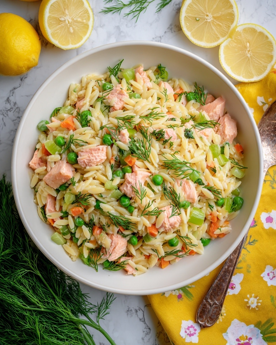 A white bowl filled with a mix of light golden orzo pasta, small chunks of pale pink salmon, and bright green celery pieces, all topped with fresh green dill sprigs scattered evenly on top. The bowl sits on a white marbled surface, with two fresh lemon slices on the upper right side and a vibrant yellow cloth with white flower patterns behind the bowl. A small bunch of fresh dill lies to the bottom left of the bowl. The overall look is bright and fresh, with a mix of soft textures and colors that contrast well. Photo taken with an iphone --ar 4:5 --v 7