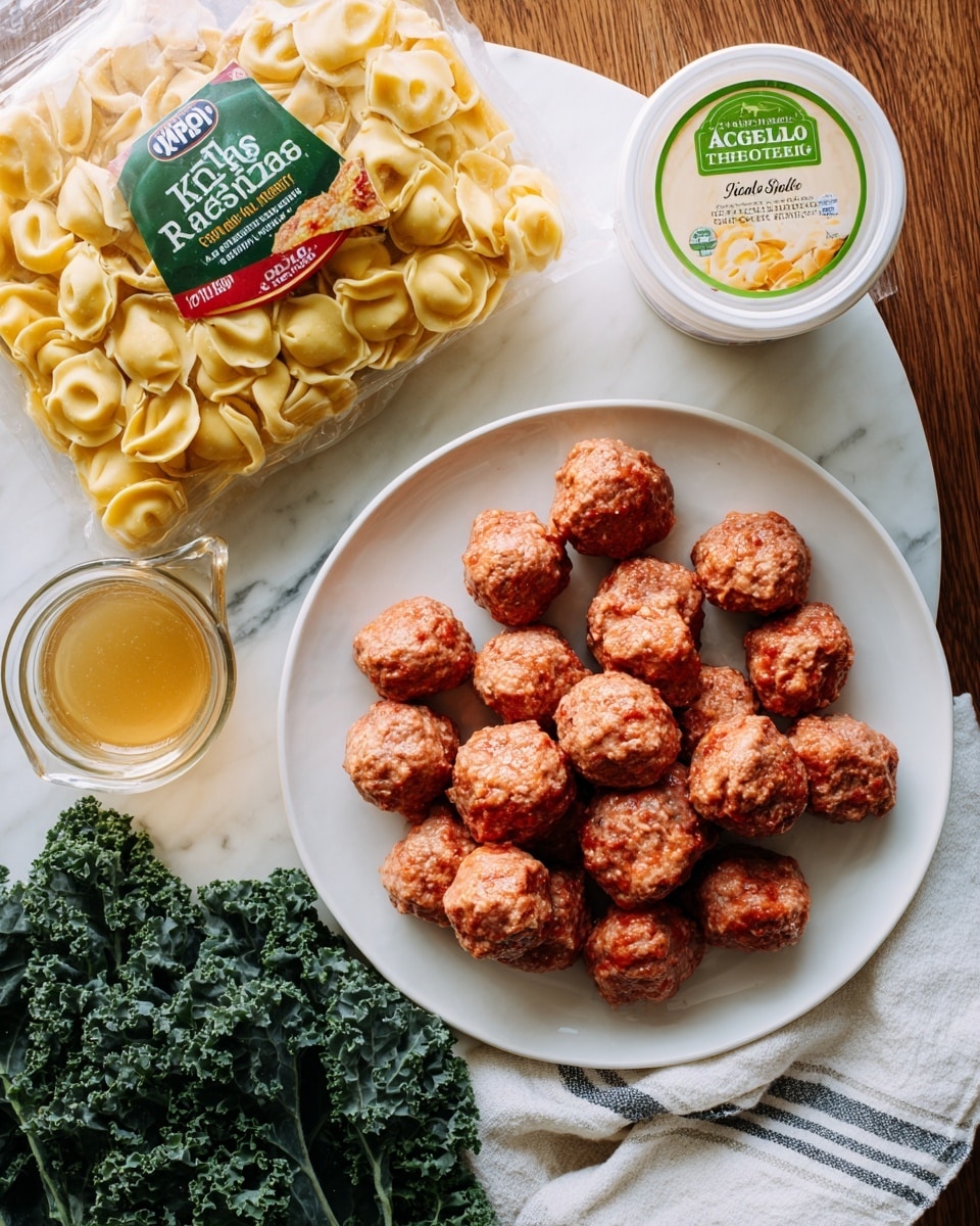 The image shows a white plate full of small meatballs with a reddish color and textured surface, placed on the top right. Below it is a white container of Alfredo sauce with a green lid. To the left, there is a clear package of yellow three cheese tortellini pasta with a bright green and red label showing the brand name. On the bottom left, a glass measuring cup contains a golden broth. Fresh dark green curly kale leaves occupy the bottom right corner. Everything is laid on a white marbled surface with a wooden background, and a white towel with a gray stripe is partly under the pasta package. Photo taken with an iphone --ar 4:5 --v 7