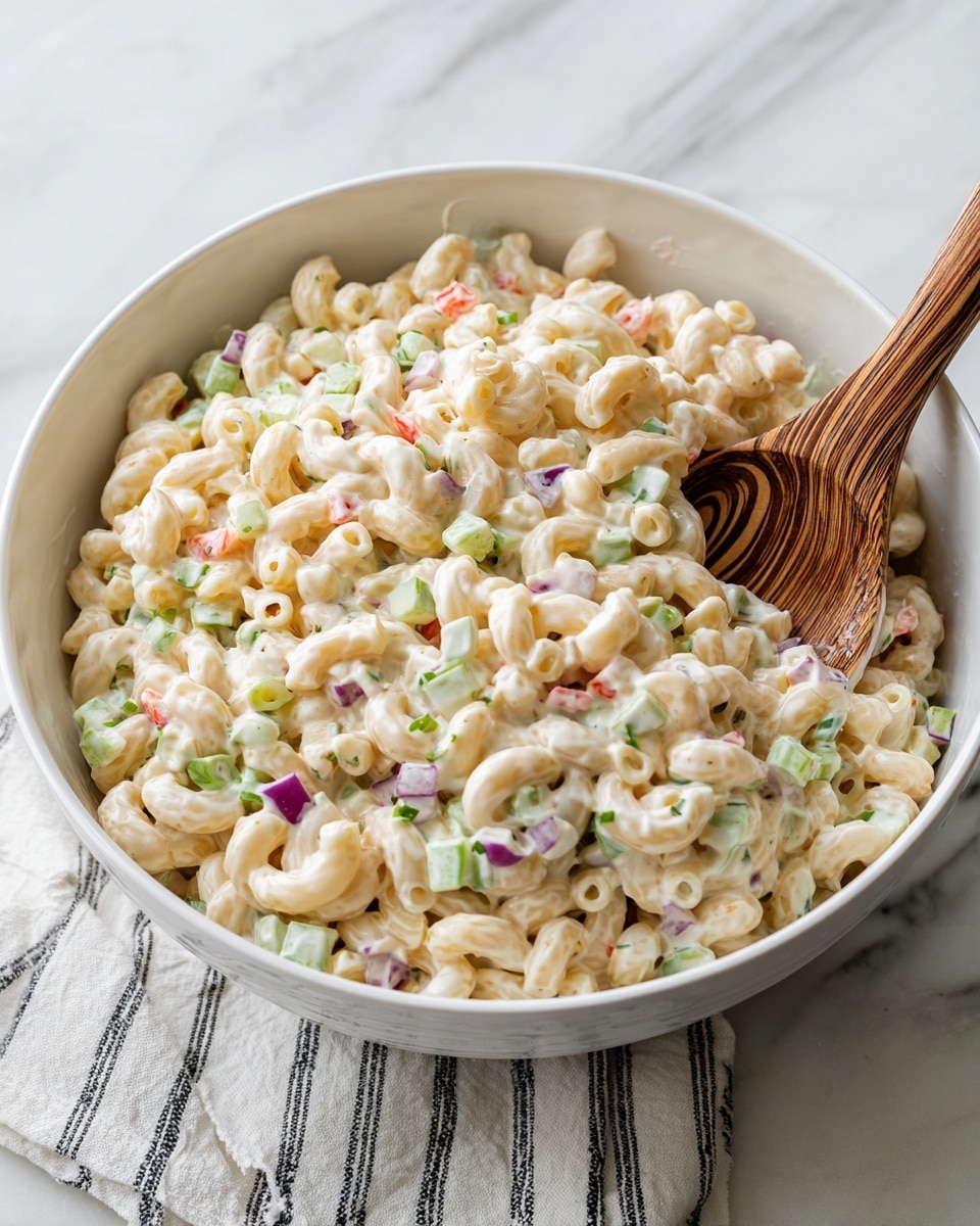 A white bowl filled with a creamy macaroni salad showing three main layers: the pasta, light cream sauce, and small pieces of diced vegetables. The bottom layer consists of pale yellow curled macaroni, softened but firm. The middle layer is a rich, thick, white creamy dressing coating the pasta completely. Scattered throughout and on top are small diced vegetables including green celery, red bell peppers, and bits of purple onion, giving tiny spots of color. A wooden spoon with a swirling grain pattern rests inside the bowl, partially covered by the salad. The bowl is set on a white marbled surface with a white cloth showing black stripes nearby. photo taken with an iphone --ar 4:5 --v 7