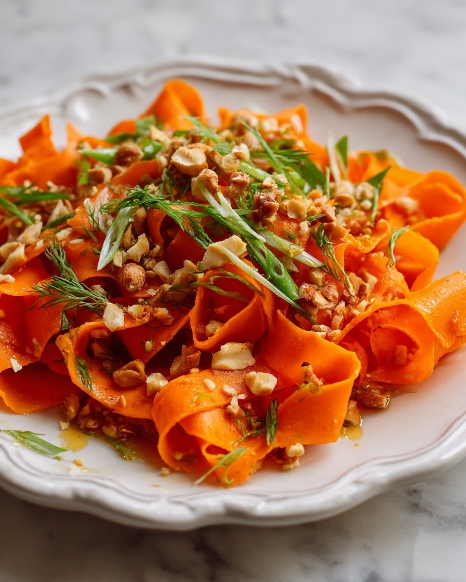 The dish is served on a white plate with wavy edges, placed on a white marbled surface. It has one main layer of bright orange carrot ribbons that are wide and curled, giving a ribbon-like texture. On top of these ribbons, there is a layer of chopped nuts, scattered evenly, adding a rough texture. Thin green slices of fresh herbs and green onions are sprinkled over the nuts, adding fine, fresh details and a splash of green color. The dish has a slight shine from a light sauce or dressing coating the carrots, making the carrots look moist and fresh. photo taken with an iphone --ar 4:5 --v 7