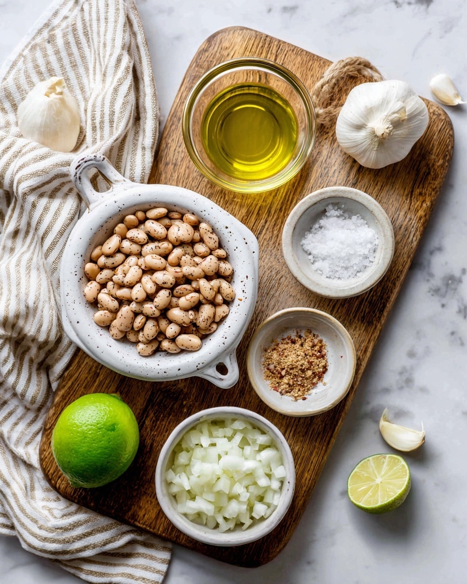 The image shows a wooden board on a white marbled surface. On the board, there is a white sieve with light brown speckled beans, a small clear glass bowl with green olive oil, a larger white bowl with chopped white onions, a smaller white bowl with small pieces of garlic, another small bowl with light brown spice powder, and a clear bowl with pink salt. A whole green lime and a white garlic bulb are also on the board. A striped beige and white cloth is placed on the white marbled background next to the board. photo taken with an iphone --ar 4:5 --v 7