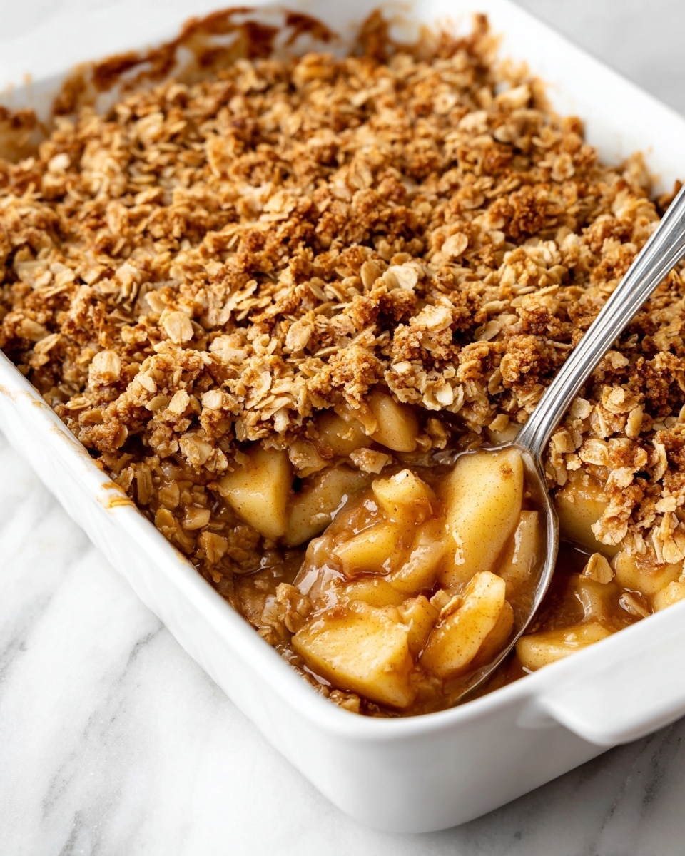 The image shows two white bowls filled with apple crisp. Each bowl has a layered look with caramel-colored baked apple chunks mixed with golden brown crumbly topping on top, giving a crunchy texture. The apple pieces are soft and shiny, coated in a syrupy glaze that adds a sticky look, while the topping is dry and crumbly with a light brown color. One bowl sits in the front on a folded green cloth on a white marbled surface, and the other is placed slightly behind it. A steel spoon is to the right of the front bowl. Photo taken with an iphone --ar 4:5 --v 7