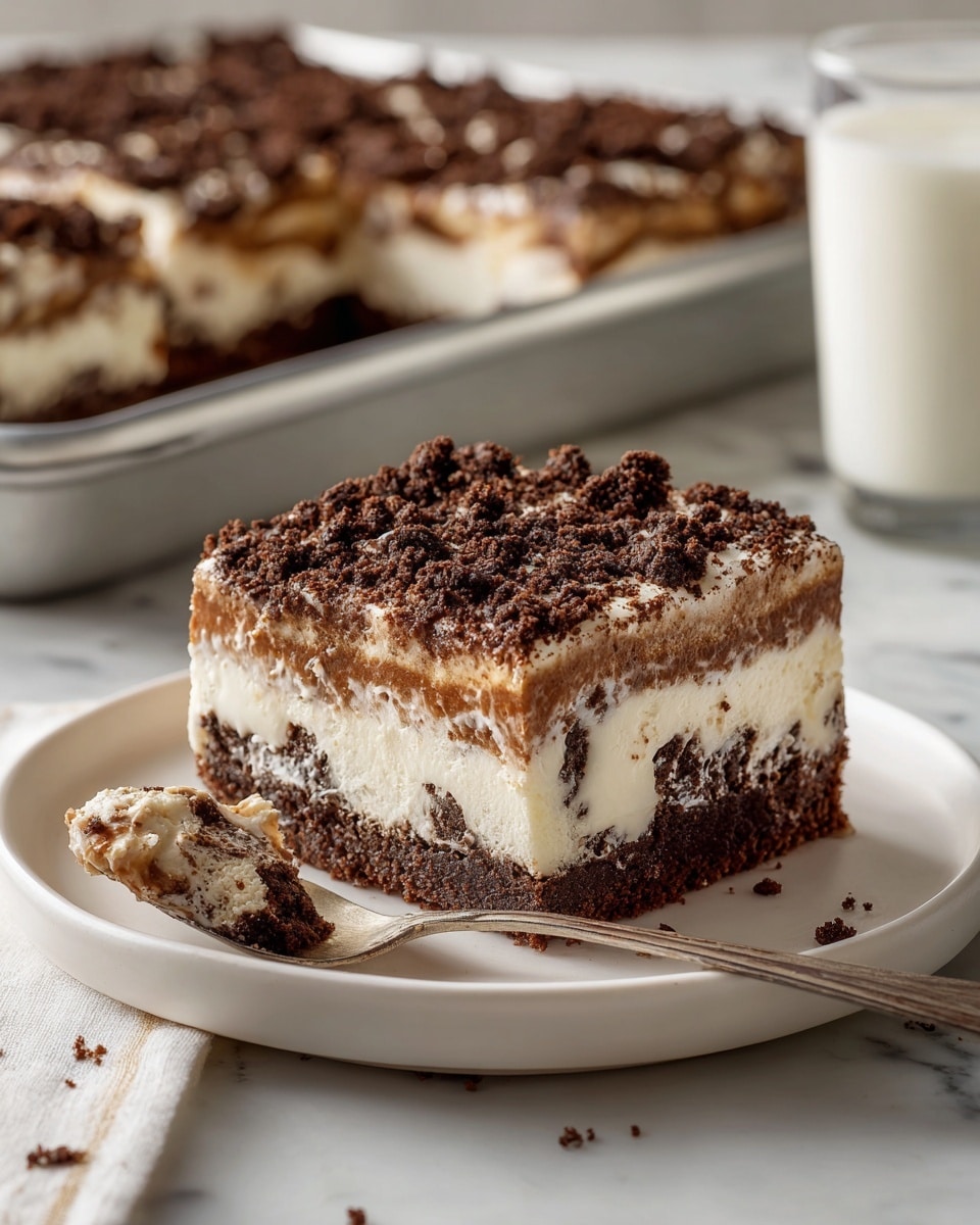 A square dessert piece sits on a white plate with a spoon holding a partly eaten section beside it. The dessert has three layers: the bottom layer is dark and crumbly, the middle layer is a thick, pale cream with chunks visible inside, and the top layer is a lighter brown cream covered with dark, crumbly bits that look like cookie crumbs. The plate is on a white marbled surface, with a tray of more dessert pieces in the background and a glass of milk on the side. Photo taken with an iphone --ar 4:5 --v 7