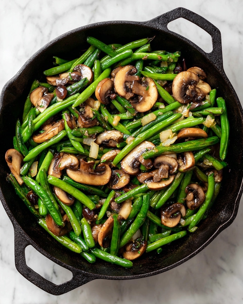 The image shows a black cast iron pan filled with cooked green beans cut into short pieces mixed with sliced brown mushrooms. The green beans have a bright green color and firm texture, while the mushrooms are soft with a light brown and tan color. There are small bits of cooked garlic and onions scattered evenly throughout the vegetable mix. The pan is set on a white marbled surface, and the scene is captured from above, highlighting the vibrant colors and textures of the veggies, photo taken with an iphone --ar 4:5 --v 7