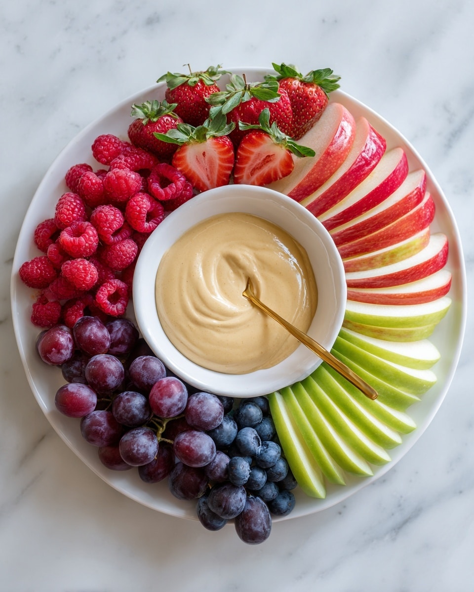 A white round plate arranged with three layers of apple slices around the edge, alternating green and red colors creating a colorful ring. Inside this ring, sliced strawberries with green leaves are placed next to a small cluster of blue grapes and fresh red raspberries at the top. In the center of the plate, a smaller white bowl holds a creamy, smooth beige dip with a golden spoon resting inside it. The plate is placed on a white marbled surface. photo taken with an iphone --ar 4:5 --v 7