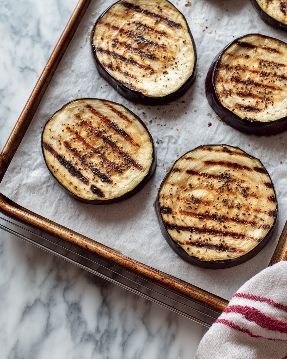 Four large slices of roasted eggplant are spread out on a baking sheet with a slightly browned metal edge. The eggplant slices are light brown with darker grill marks and some black pepper sprinkled on top. The eggplant skin is dark purple and frames each slice. The baking sheet rests on a metal cooling rack and a white marbled surface with part of a white and red kitchen towel visible on the side. photo taken with an iphone --ar 4:5 --v 7
