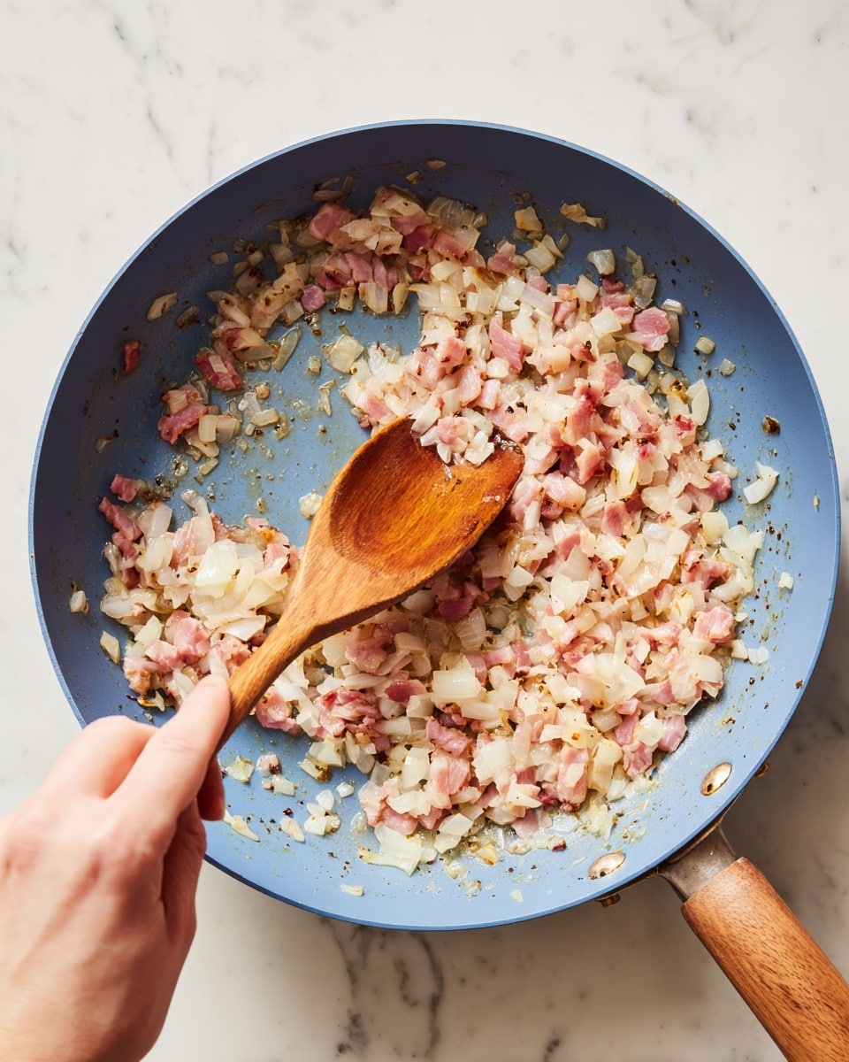 A blue pan filled with many small pieces of cooked onions and pink bacon, softly mixed and slightly shiny with cooking oil. A woman’s hand is holding a wooden spoon stirring the ingredients in the pan. The pan has a wooden handle and sits on a smooth white marbled surface. The ingredients show soft pink and white colors with some light brown bits, filling most of the pan’s round space. Photo taken with an iphone --ar 4:5 --v 7