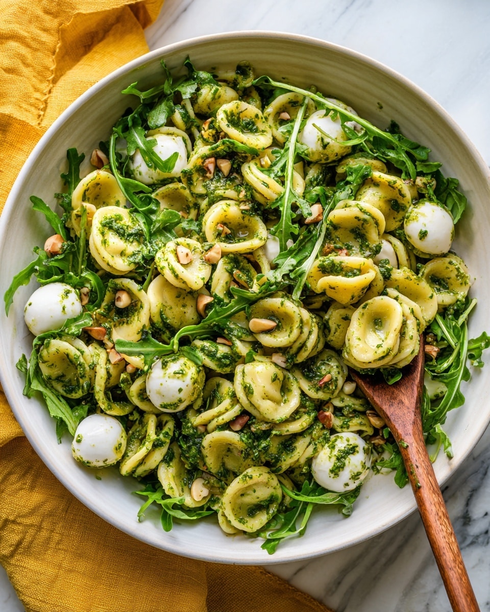 A white bowl filled with pasta shaped like small rings, mixed with green vegetables like asparagus and peas, along with white small mozzarella balls. The pasta and vegetables are coated in a creamy, light green sauce with visible small herbs. A wooden spoon rests inside the bowl, partially covered by the pasta. The bowl is placed on a white marbled surface, and next to it, there is a small white plate with chopped green herbs sitting on a yellow cloth napkin. Photo taken with an iphone --ar 4:5 --v 7