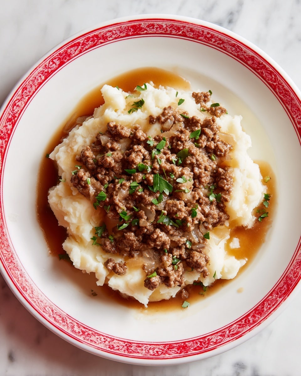 The dish shows two layers on a white plate with red patterns along the edge. The bottom layer is creamy mashed potatoes, spread unevenly with a fluffy texture and soft white color. The top layer is a generous scoop of browned ground meat in a glossy brown sauce mixed with small pieces of onion, scattered with green parsley leaves for color. The mashed potatoes form a border around the meat, which sits in the center. The plate is placed on a white marbled surface. Photo taken with an iphone --ar 4:5 --v 7