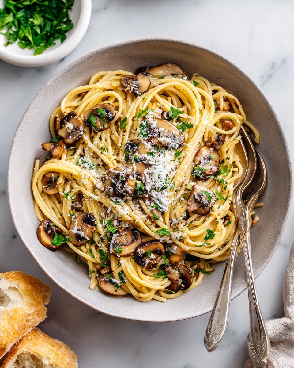 A cast iron pan filled with creamy spaghetti pasta mixed with sautéed brown and golden mushrooms spread evenly throughout. The spaghetti strands are light yellow and soft, coated in a creamy white sauce with finely chopped green herbs sprinkled on top, along with a light dusting of grated cheese and cracked black pepper. The pan has a white handle and sits on a beige cloth over a white marbled surface, with a silver fork and spoon resting inside the pan. Nearby, there is a small white bowl with fresh green leafy herbs and a wooden-handled knife next to small chunks of Parmesan cheese. Photo taken with an iphone --ar 4:5 --v 7