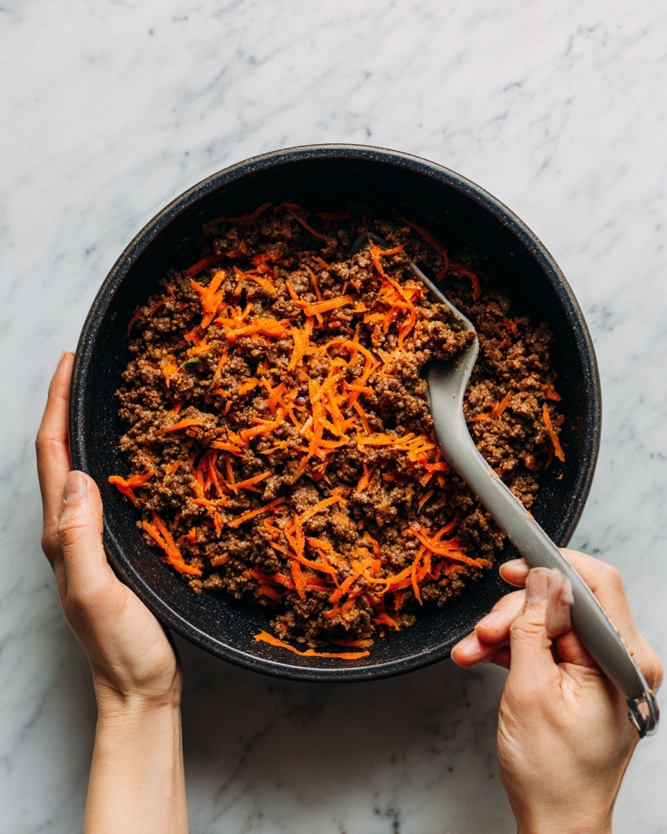 A close-up top view of a black mixing bowl held by two woman's hands over a white marbled surface, filled with a thick mixture of raw ground meat and shredded orange carrots, with a gray spatula resting inside the bowl partially covered in the mixture photo taken with an iphone --ar 4:5 --v 7