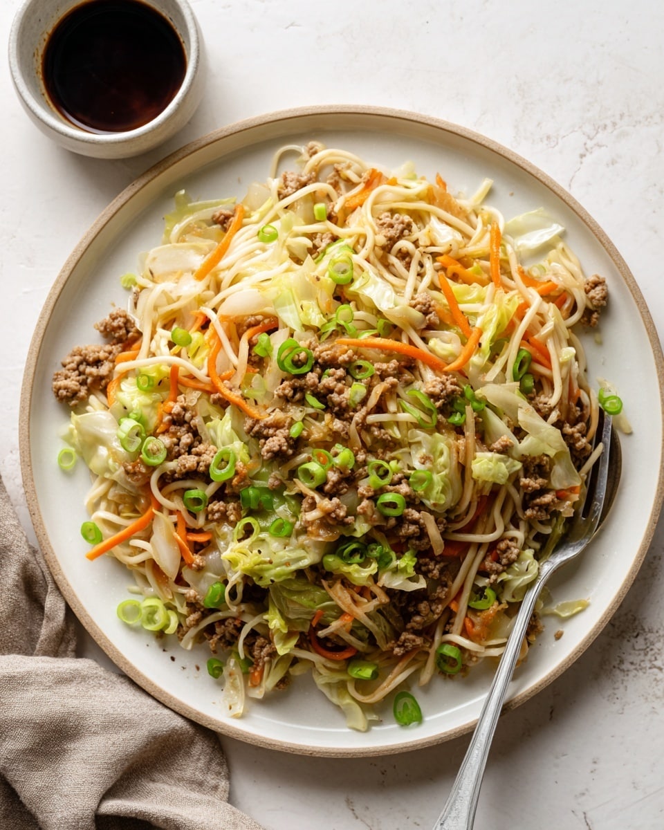 A white plate filled with a colorful noodle dish featuring three main layers: the bottom layer is light green cabbage, the middle layer contains light orange thin carrot strips, and the top layer has white noodles mixed with small bits of light brown cooked ground meat and some green onion slices. A silver fork rests inside the plate on the right side. There is a small white bowl with a dark sauce on the left side of the white marbled surface background. photo taken with an iphone --ar 4:5 --v 7