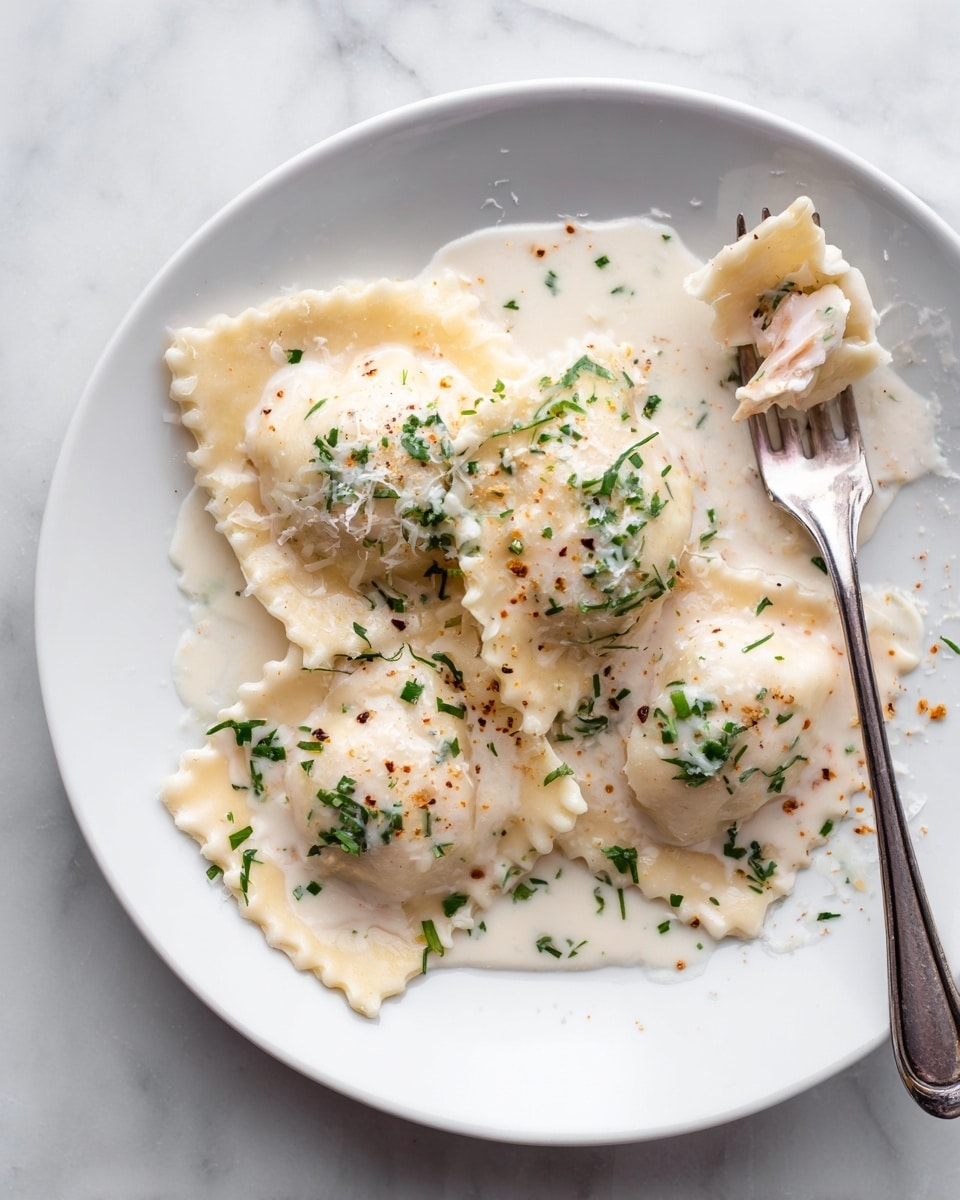 A white plate contains four ravioli pieces with creamy white sauce drizzled over them, some herbs sprinkled on top, and some grated cheese. One ravioli is broken open, showing a light pink filling inside. A silver fork rests beside the ravioli with its tines touching the sauce. The plate sits on a white marbled surface. photo taken with an iphone --ar 4:5 --v 7