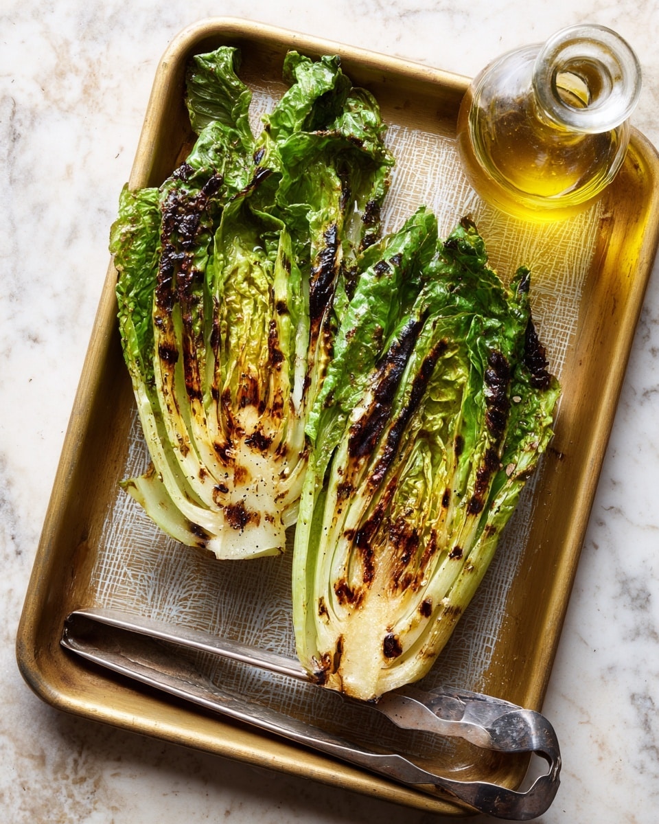 Two halves of grilled romaine lettuce lie side by side on a gold baking tray with a matte textured pattern. Each lettuce half shows a gradient of color from light green at the base to a darker, leafy green at the top, with charred brown grill marks on the cut side. A silver metal tong rests below the lettuce halves on the tray, and a small glass bottle filled with golden olive oil is placed to the tray’s top right. The background surface is a white marbled texture. photo taken with an iphone --ar 4:5 --v 7