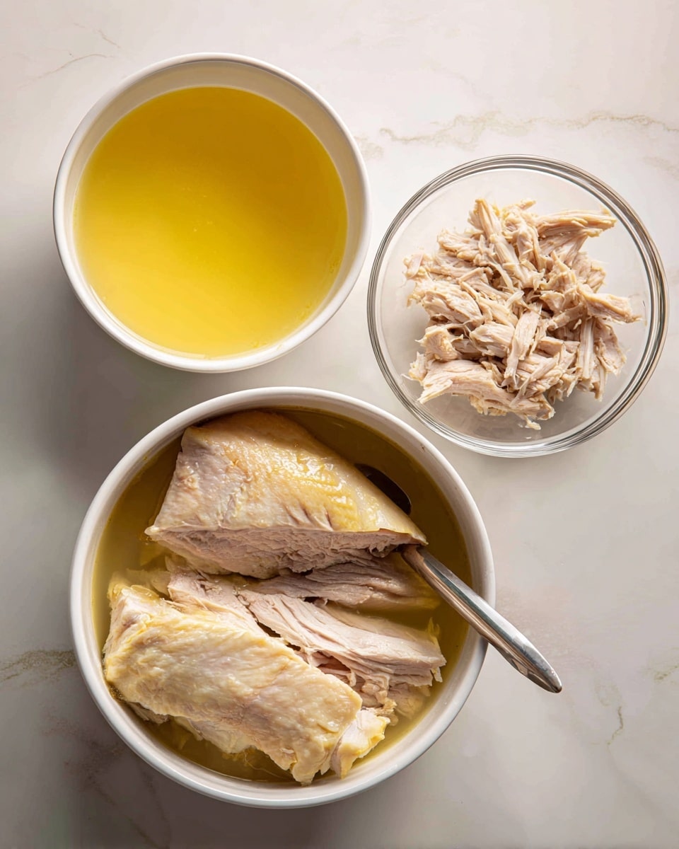 A white pot filled with clear yellow broth sits on a white marbled surface, next to two clear glass bowls. The bowl on the top right contains light beige shredded meat, while the larger bowl below it holds a large cooked piece of light beige meat with some skin showing, with a metal tool partially inserted into it. The white marbled surface has faint grey veins and the overall scene looks clean and bright, with soft lighting highlighting the textures and colors of the broth and meat photo taken with an iphone --ar 4:5 --v 7