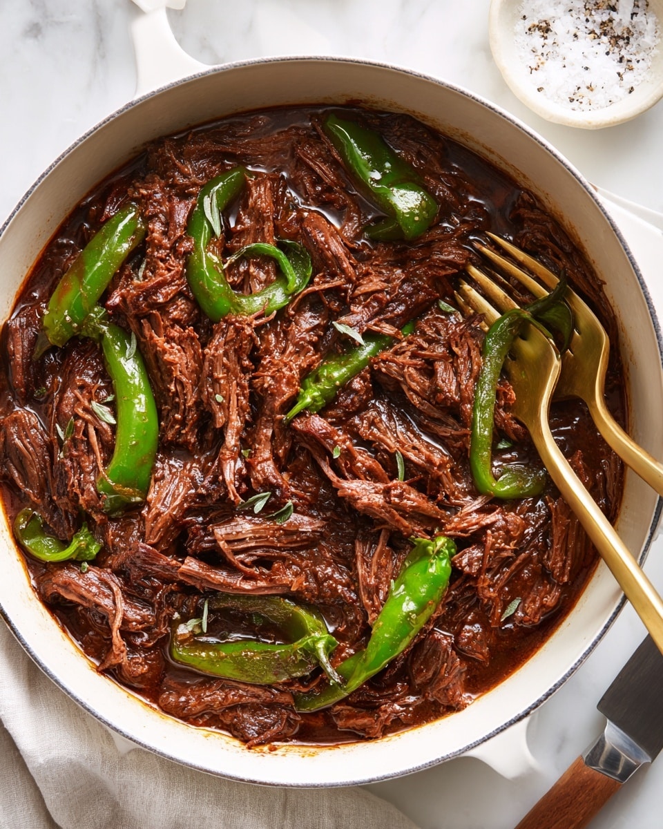 A close-up view of a white cast iron pot filled with shredded dark brown beef in thick, shiny brown sauce, mixed with whole roasted green peppers scattered evenly through the meat. Two golden forks inserted into the beef pull some strands up, emphasizing the tender texture. The pot sits on a white marbled surface with a knife on the lower right and a small round white dish filled with salt and pepper partially visible in the top right corner. Photo taken with an iphone --ar 4:5 --v 7