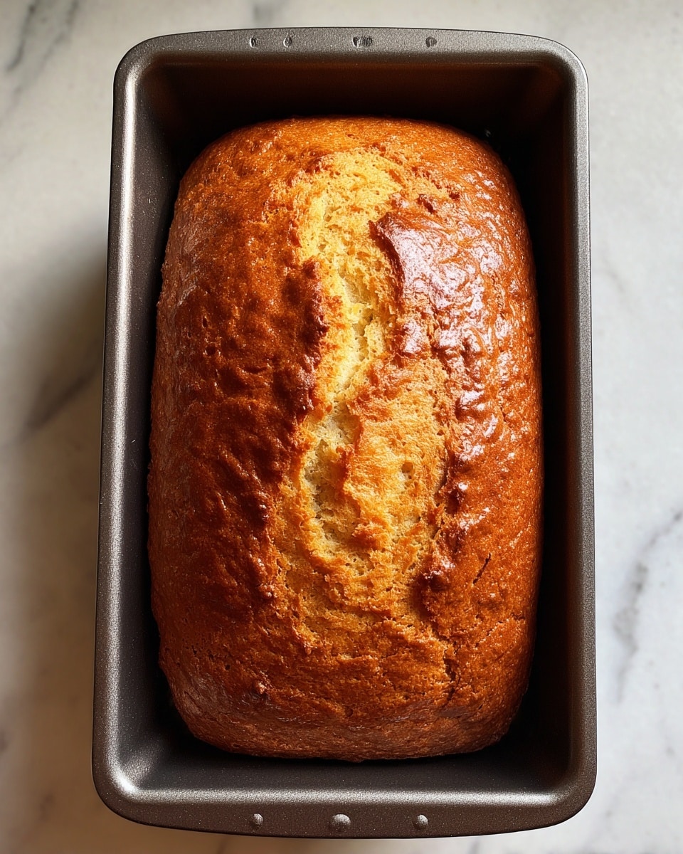 The image shows a loaf of brown cake on a white plate, sliced into four pieces. The bottom slice is the largest and still attached to the main loaf, with a shiny textured top and moist inside. Above it are three evenly cut slices, each with a soft, spongy texture and slightly darker crust edges. The cake's color varies from a medium golden brown inside to a darker brown crust. The white plate sits on a white marbled surface, highlighting the cake’s warm tones. photo taken with an iphone --ar 4:5 --v 7