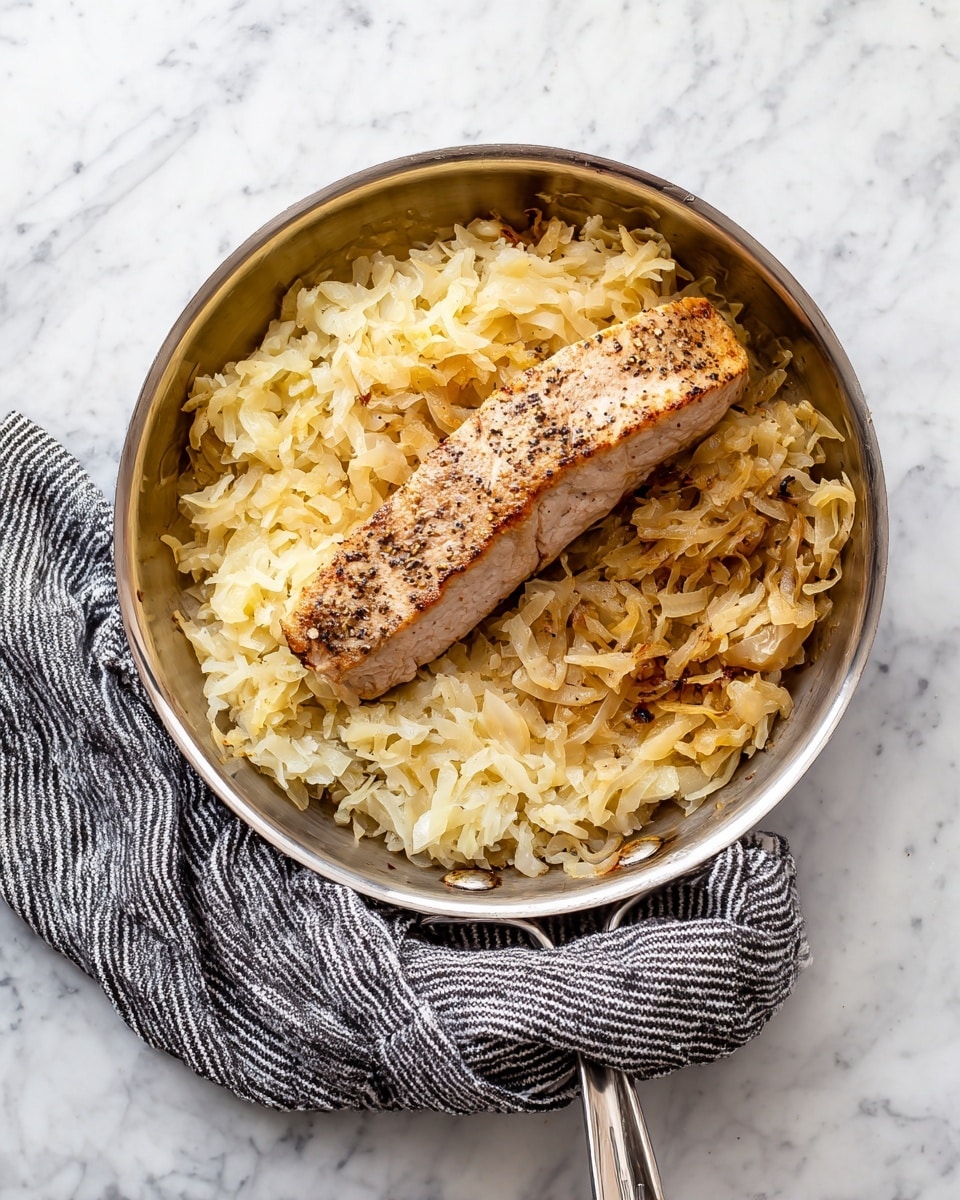 A white plate holds two sliced pieces of cooked pork tenderloin with a light brown outside and a pale pink inside, arranged on a bed of cooked sauerkraut that is light golden and slightly translucent. The plate is placed on a white marbled textured surface with a beige cloth with black stripes at the top left. To the right, there is a white rectangular dish filled with small, light yellow spaetzle pasta pieces. photo taken with an iphone --ar 4:5 --v 7